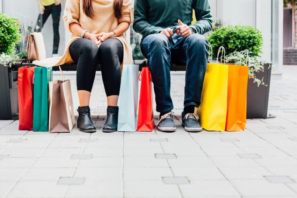 Couple sitting on a bench with colorful shopping bags, reflecting changing consumer behavior in retail.
