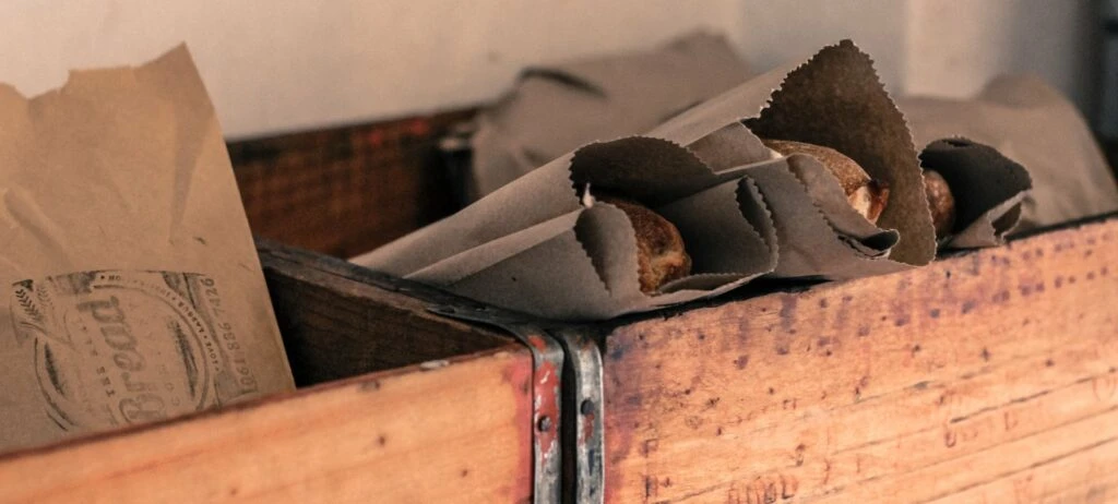 Brown paper bags with bread loaves in a wooden crate, highlighting sustainable packaging practices in the food industry.