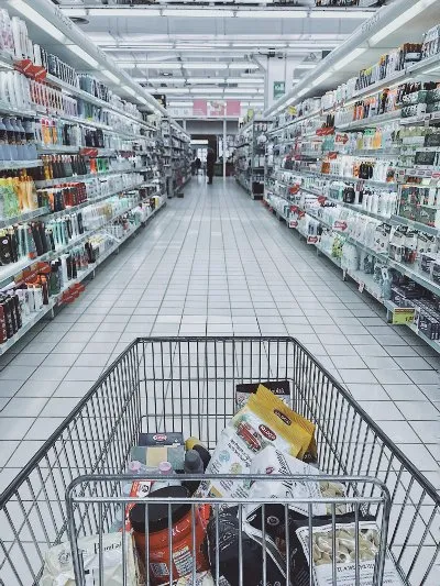 Shopping trolley filled with various products in a supermarket aisle, highlighting consumer interest in sustainable packaging and eco-friendly options.