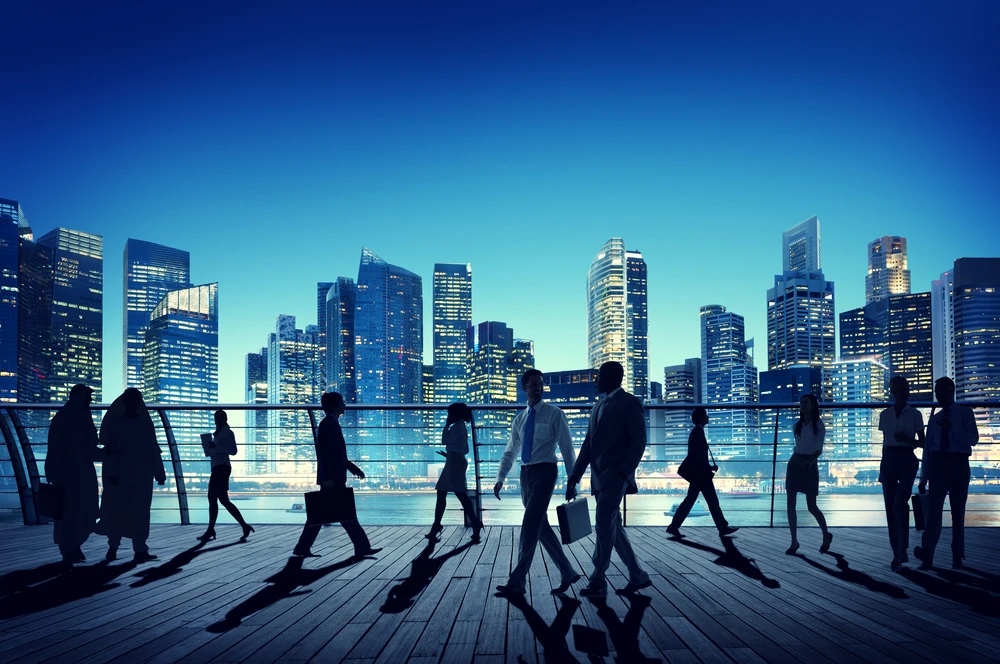 Silhouettes of diverse business professionals walking along a waterfront promenade with a modern city skyline at dusk, representing B2B branding and market research themes.