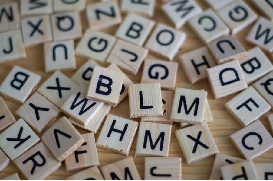 Wooden letter tiles scattered on a surface, featuring various uppercase letters, representing language and semiotic cues in marketing communication.