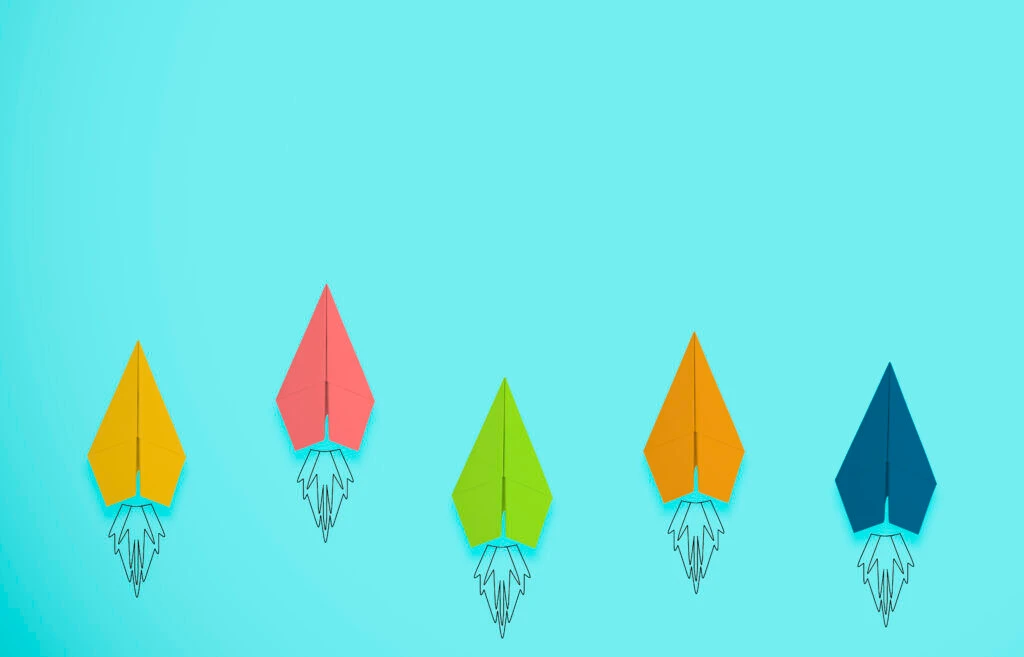 Colorful paper rockets in varying shades of yellow, pink, green, orange, and blue against a light blue background, symbolizing innovation and progress in qualitative research methods.