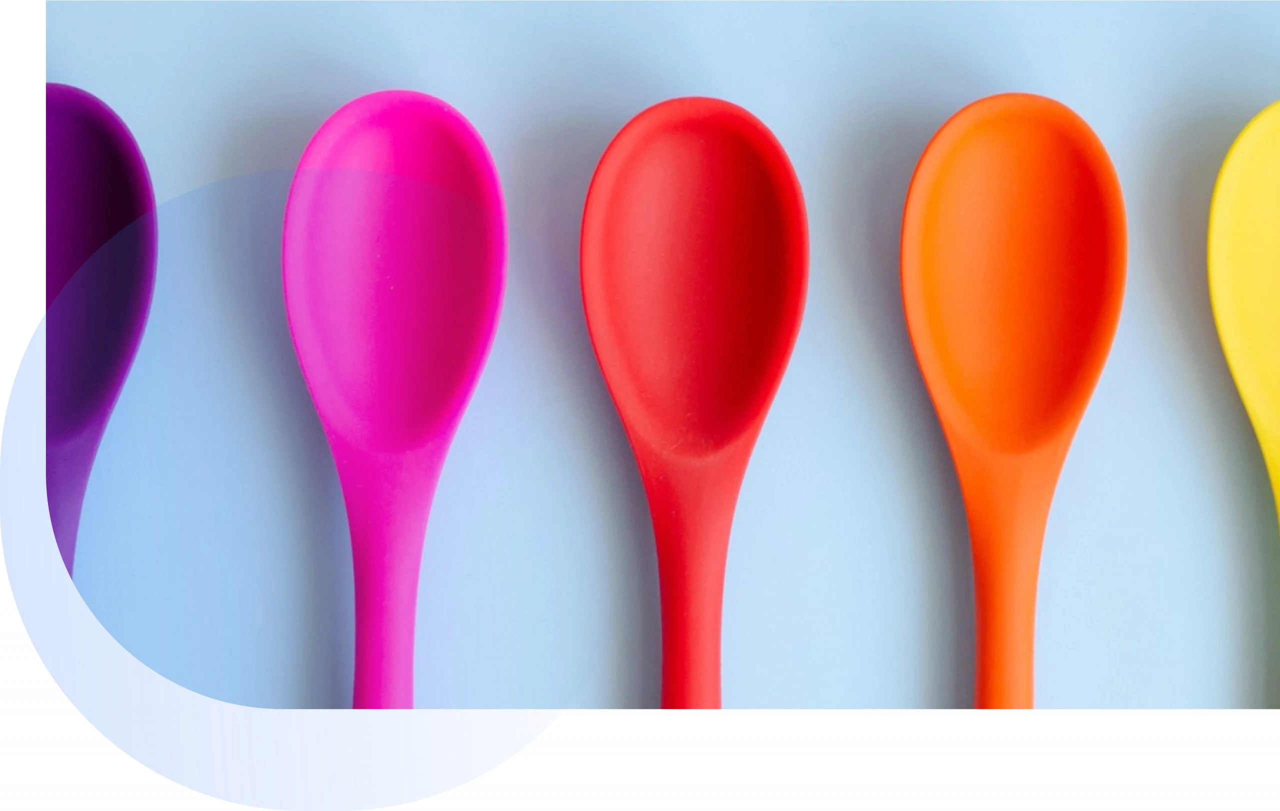 Colorful silicone spoons in purple, pink, red, orange, and yellow arranged in a row against a light blue background, representing vibrant kitchen utensils for market research in consumer preferences.