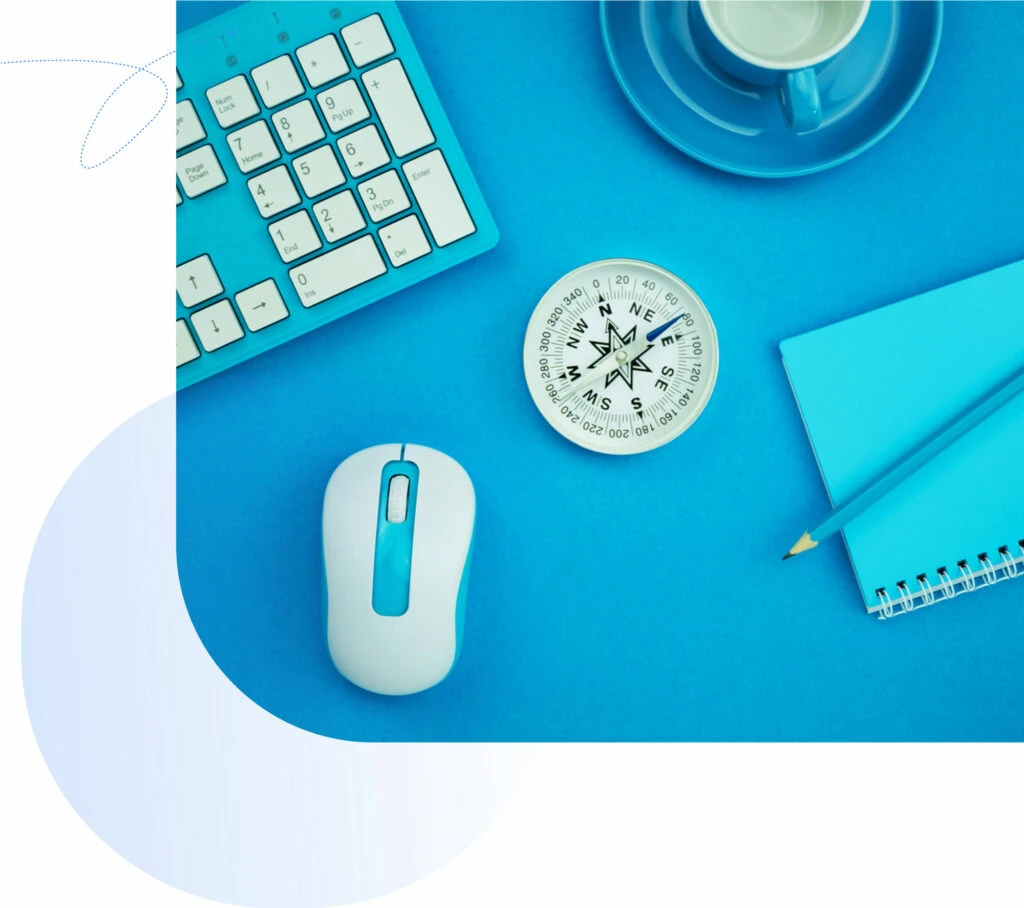 Blue keyboard and mouse, compass, notebook, and cup on a blue background, symbolizing digital marketing and strategic guidance for Brandspeak's data processing services.