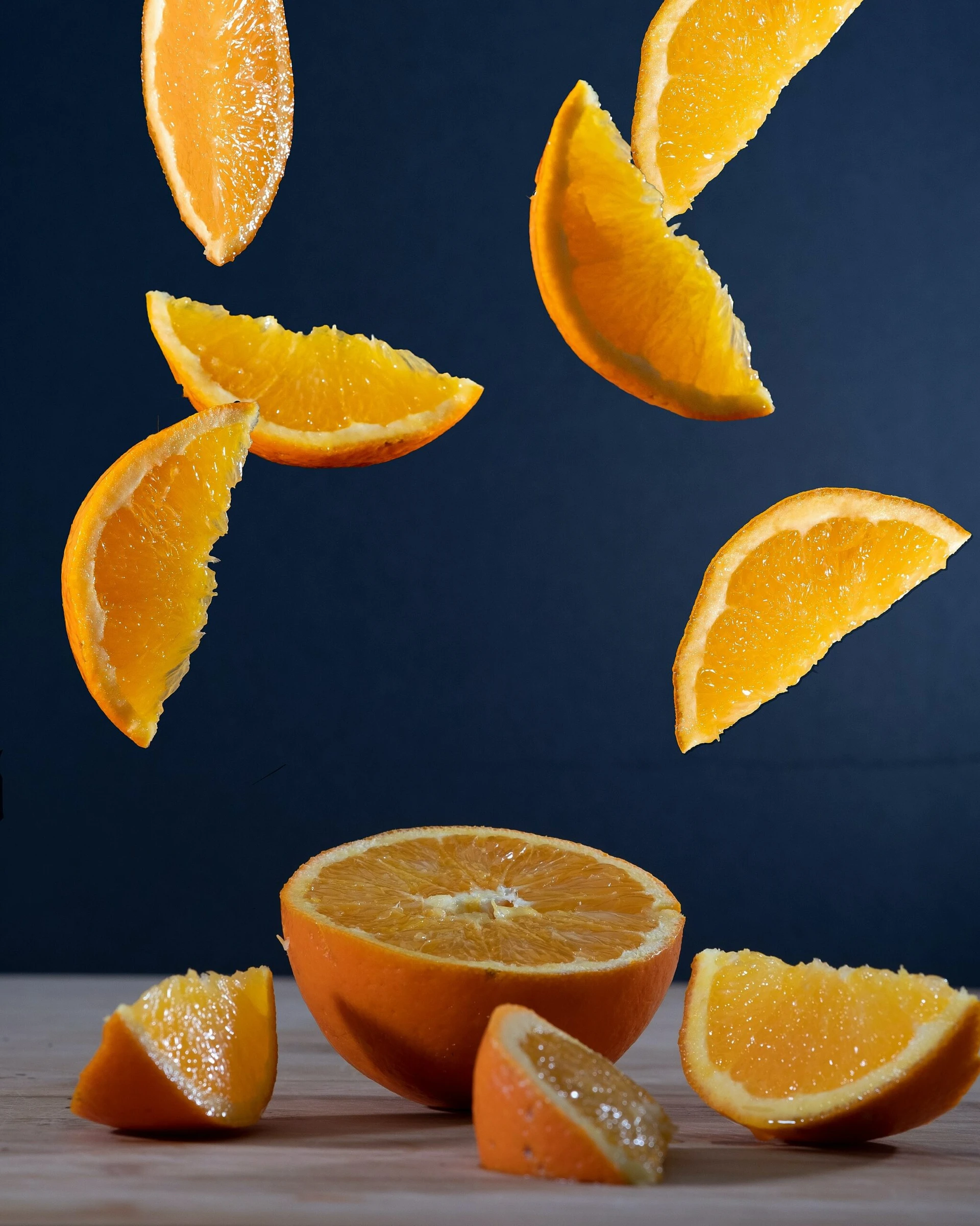 Sliced orange segments floating above a halved orange on a wooden surface, against a dark background, emphasizing freshness and vibrant color.